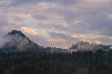 Mountains and peaks in fog at sunrise or sunset. Sun from behind the mountain. Amazing view of mountains and forest landscape with cloudy skies Altai mountains. Mountains and peaks in fog at sunrise