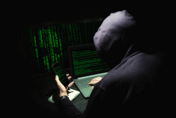 Hacker encapuchado cometiendo un ciberataque con varias pantallas en las que se ven códigos informáticos. Robo de datos. - obrazy, fototapety, plakaty