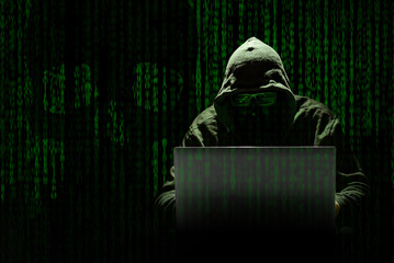 Un hacker encapuchado trabaja en un ciberataque sobre un fondo de código informático donde se aprecia una calavera. Concepto criminalidad de los delitos informáticos en la era digital. - obrazy, fototapety, plakaty