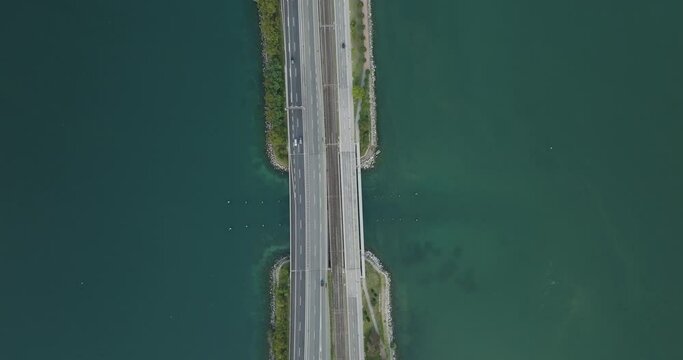Aerial view of vehicles driving on a road crossing the Lugano lake with a bridge and a boat sailing under the bridge, Melide, Ticino, Switzerland.