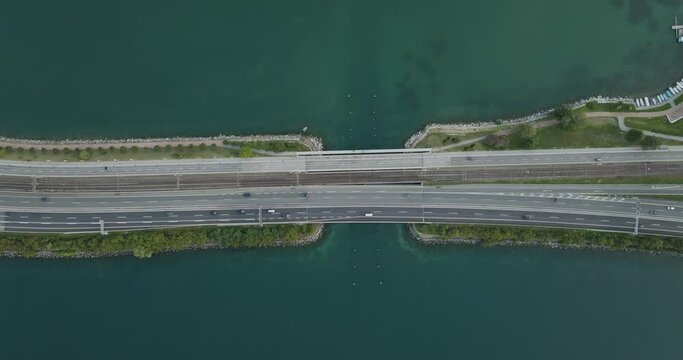 Aerial view of vehicles driving on a road crossing the Lugano lake with a bridge and a boat sailing under the bridge, Melide, Ticino, Switzerland.