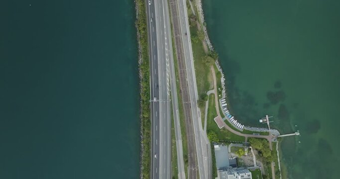 Aerial view of vehicles driving on a road crossing the Lugano lake with a bridge and a boat sailing under the bridge, Melide, Ticino, Switzerland.
