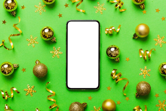 Christmas online shopping from home phone with blank white display top view. smart mobile with copy space on colored background with Christmas decorations balls,. Winter holidays sales background