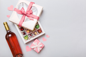 Bottle of red wine on colored background for Valentine Day with gift and chocolate. Heart shaped...