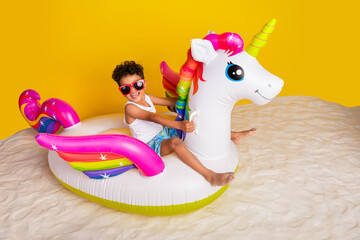 Full length photo of excited funky small boy wear white shirt swimming floating unicorn matrass isolated yellow color background