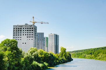 New apartment buildings under construction on banks of river. Tower crane during construction