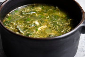 Soup with green sorrel in black ceramic pot on gray background