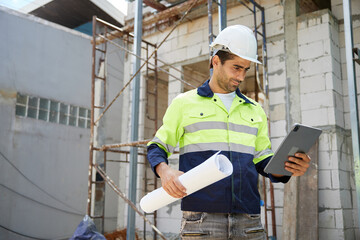 worker or architect holding blueprint paper and working on tablet at construction site