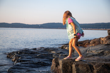 Girl crouching on rock at edge of lake, Lake Superior