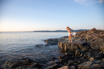 Girl on rock at edge of lake at sunrise, throws rock into lake, Lake Superior