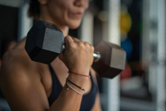 Close up, fitness girl lifting dumbbell weights at the gym, doing exercises with dumbbell, fitness muscular body, selective focus