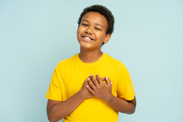 Smiling African American teenager wearing stylish casual yellow t shirt holding hands on heart
