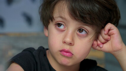 Close-up child face with bored expression. Pensive small boy struggles with boredom gazing in the...