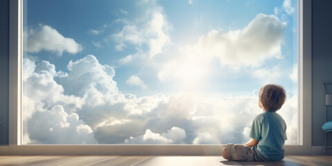 A boy is daydreaming sitting by a large window. He looks at the sun and the clouds. Wide format.