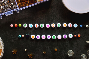 Friendship bracelet letter beads and various other jewelry making supplies on dark background. Top view.