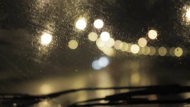 Rain On Windshield, Blurred Lights seen from Inside a Car During Rainy Night. Close Up.
