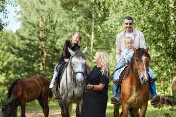 Happy family: father, son, mother and daughter having fun riding horse. Outdoor fun for kids. Evening forest walk.