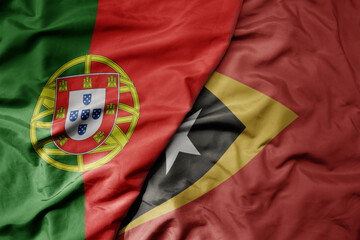 Fototapeta premium big waving national colorful flag of portugal and national flag of east timor .