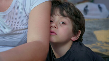Bored child hiding behind mother's arm feeling boredom, close-up of shy kid with nothing to do