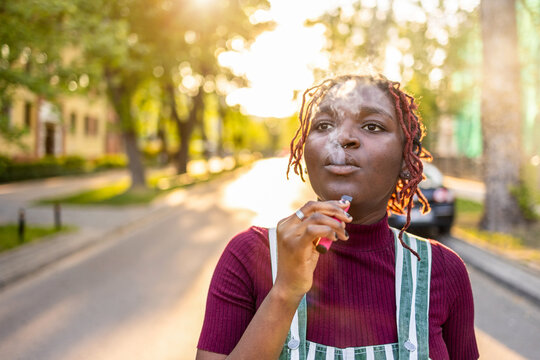 Black non-binary person smoking electronic cigarette in the street