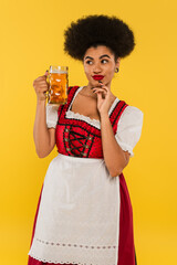 tricky african american oktoberfest waitress in dirndl costume standing with beer mug on yellow