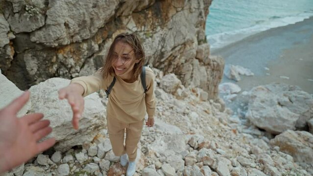 POV first person view joyful young smiling woman hiker hiking and climbing up rocky canyon at seaside and getting help. wanderlust and travel summer vacation trip. halping hand, follow me
