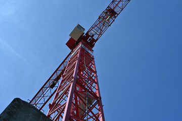 An industrial tower crane of red color with a stretched arm and a white driver cabin observed from down. The photo with a lot of copy space.