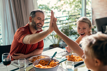 Fototapeta na wymiar Beautiful kind family celebrating and shaking hands while eating together in the kitchen at home