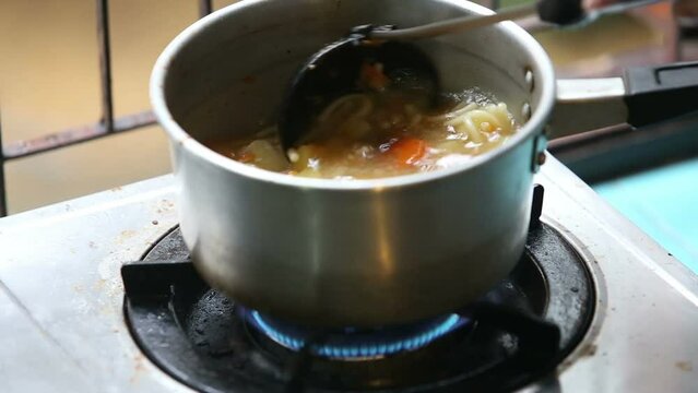 Stirred ladle chicken with noodles and potatoes cold soup in a small saucepan on the gas stove near the window