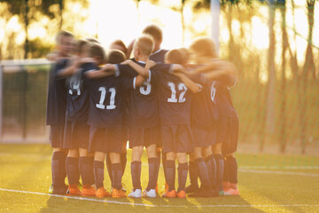 Youth sports players stand in a circle huddling together and motivating each other before the...