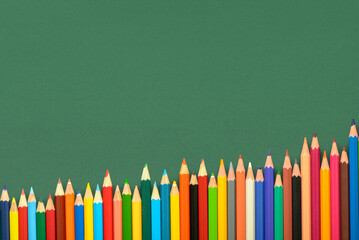 multicolored pencils on green chalkboard background, back to school concept and growth to...