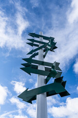 white sign post with many dark green blank arrows and a blue sky with white clouds