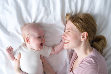 young mother hugging her baby lying on bed. top view