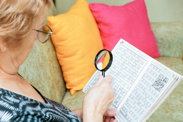 Senior woman solves crossword puzzles with a magnifying glass
