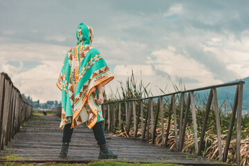 Fototapeta premium Model wearing a poncho handmade with sheep cloth by the indigenous Kichwa artisan communities of the area, posing at the San Pablo lake in Otavalo, Ecuador.