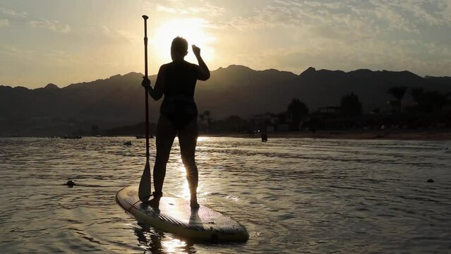Young woman dancing on the sup board at sunset in Egypt