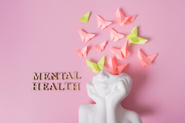 A figurine of a head with butterflies on a pink background. Mental health concept