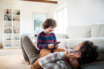 Young father playing with his son and using a smartphone in the living room at home