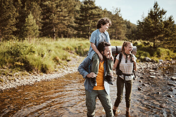 Young family crossing a creek while hiking in the forest and mountains