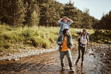 Young family crossing a creek while hiking in the forest and mountains