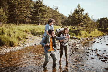 Young family crossing a creek while hiking in the forest and mountains