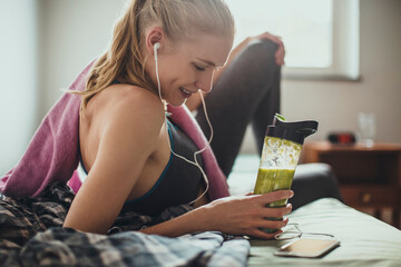 Young athletic and fit woman using a smartphone while drinking a healthy smoothie or shake after...