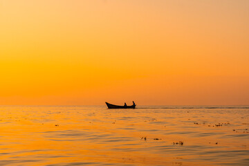 Fototapeta premium Fishing boat with a fisherman fishing in the orange sunset of Shkoder Lake in Shiroka. Albania