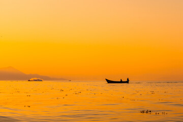 Naklejka premium Fishing boat with a fisherman fishing in the orange sunset of Shkoder Lake in Shiroka. Albania