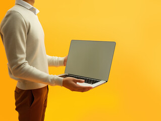 Man in causal clothing holding laptop in front of yellow background