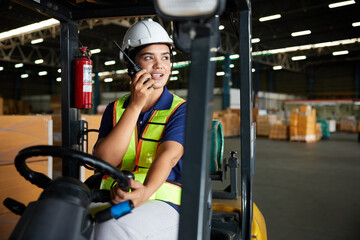 Indian worker driving a forklift and using walkie talkie in warehouse storage