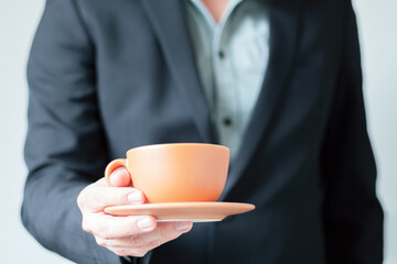 Unrecognizable businessman handing over to camera a cup of coffee and a small plate. Break at work, Espresso coffee, Caffeine.