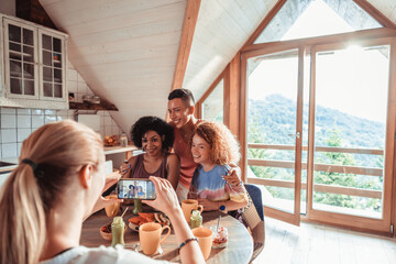 Young and diverse group of female friends taking a picture on a smartphone and having breakfast while on a holiday vacation in a cabin house