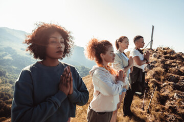 Young and diverse group of female friends doing yoga in the morning on top of a mountain after hiking