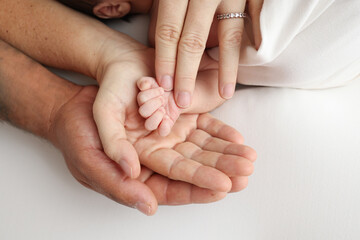 Obraz na płótnie Canvas Three palms of a happy family. Small hand of a newborn with tiny fingers, head and ear of a newborn. The palm of parents, father and mother holds the handle of a newborn. studio macro photography